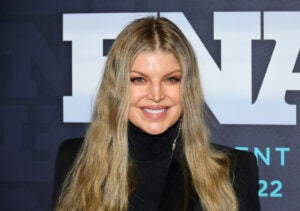 Fergie smiles at the 36th Annual Footwear News Achievement Awards with her blonde hair down wearing a black high-neck shirt