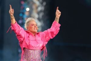 P!NK raises both hands in the air pointing up wearing a pink cropped jacket over a pink bodysuit on stage during the P!NK Summer Carnival 2023 Tour