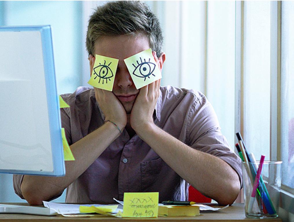 A young employee sleeps in the office hiding with posits in the eyes