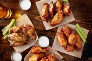 Hot wings on a wooden table. party sampler platter made to share with four different flavors of chicken wings served with beer and ranch dipping sauce. Story: Celebrities eating hot wings on Hot Ones on Youtube