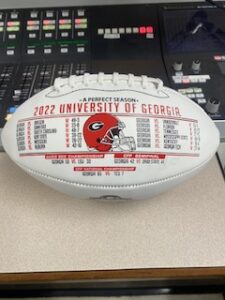 Panel 3 of a collectible UGA football in front of a radio station operating board